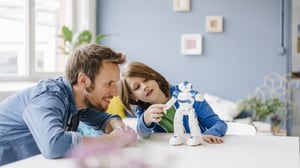 Happy father and son playing with robot on table at home